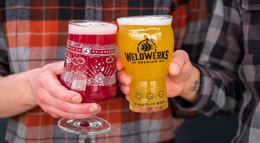 Two hands holding WeldWerks glasses toast their beers.