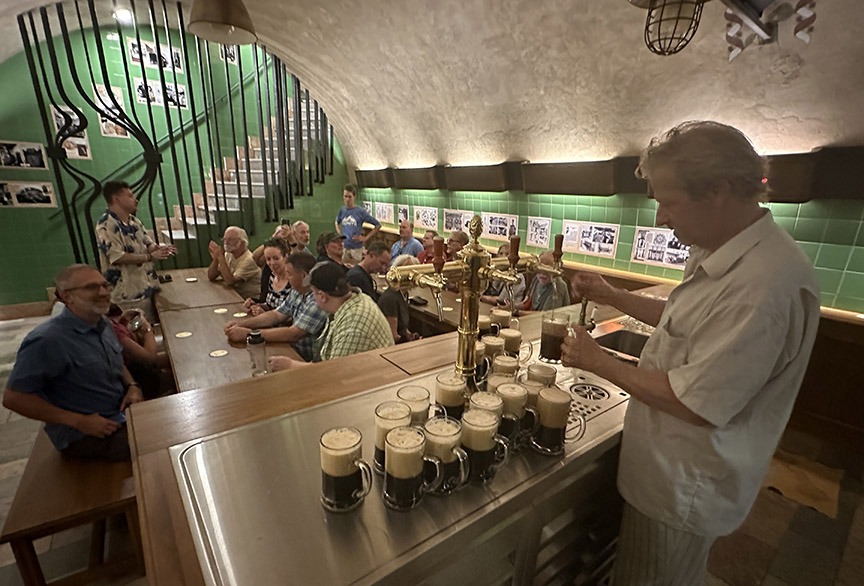 Man pours beer from a tab behind a bar in a room full of patrons.
