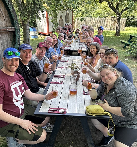 Group of people sitting at a picnic table drinking glasses of beer.