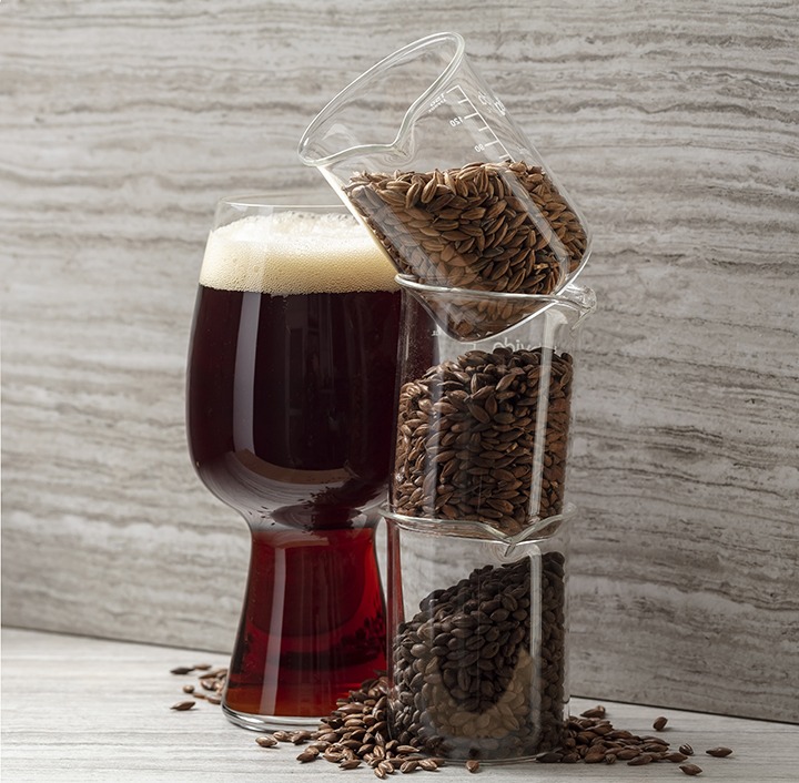 Glass of dark beer next to cups of dark malts.