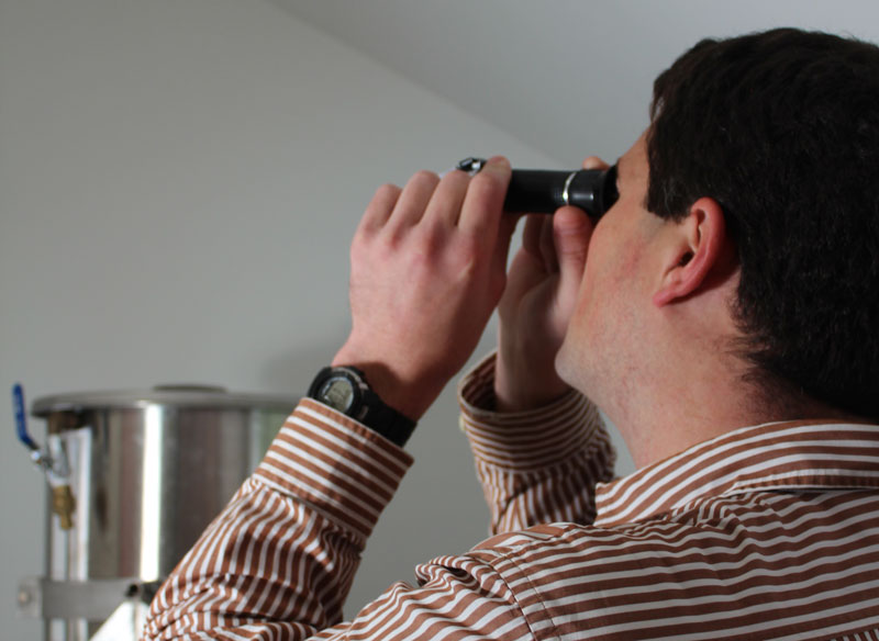 a brewer peering down the scope of a refractometer