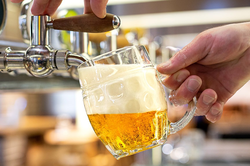 Hands pouring a lager into a glass mug from a tap.