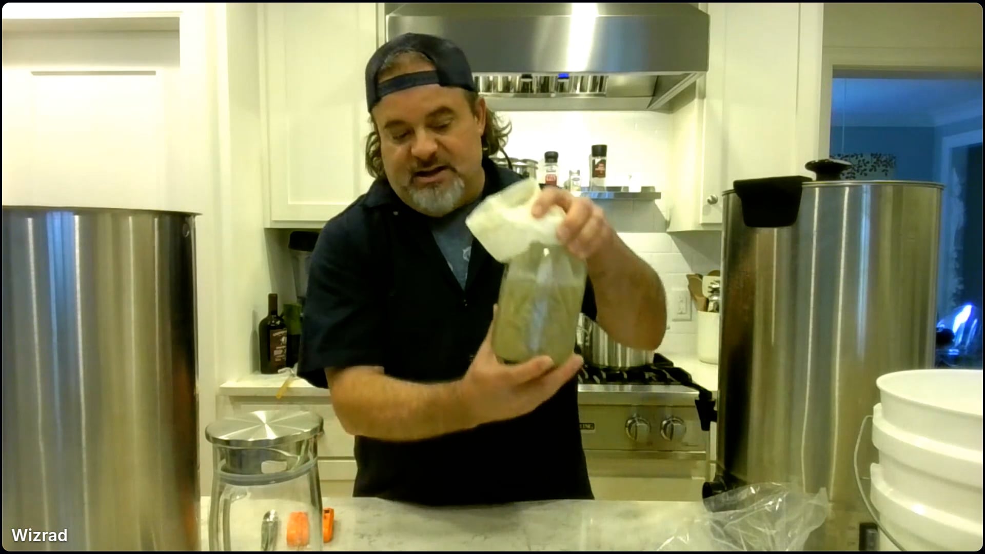 Man in kitchen with beer brewing equipment.